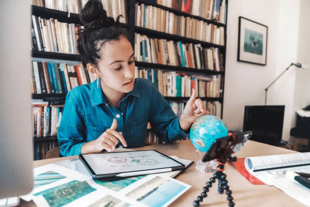 teenage girl preparing presentaion for climate change issues on digital tablet and globe teenage girl sitting at desk in front of book shelf and looking at globe and digital tablet person drawing on tablet stock pictures, royalty-free photos & images