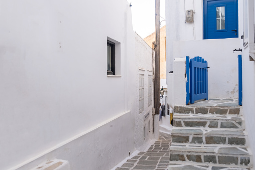 Whitewashed buildings, stone paved stairs and blue wooden fence entrance gate open. Cyclades, Greece. Ios, Nios island, Chora. Narrow cobblestone alley, traditional architecture