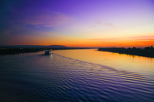 The great Nile River at sunset. In the distance, an unknown ship floats on the water. The light of the setting sun is reflected in the water.