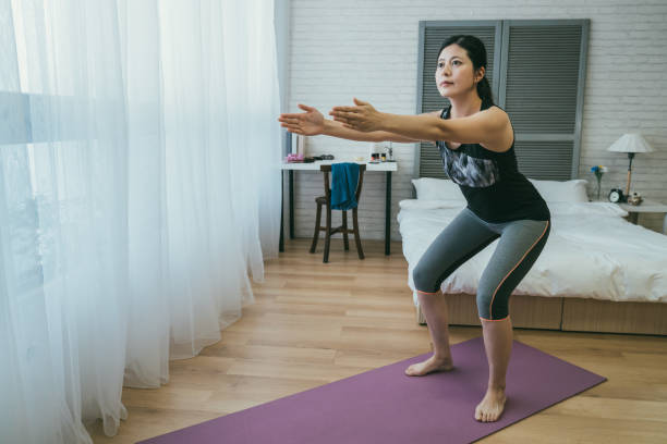 istock fit Korean female is doing squat on the exercise mat with parallel arms by the window on sunny morning in the bedroom during home workout. 1359141272