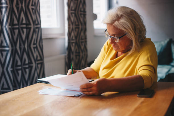 istock A senior woman is analyzing the bill in her hand, while she writes down numbers in her notebook, to calculate month expanses. 1359142780