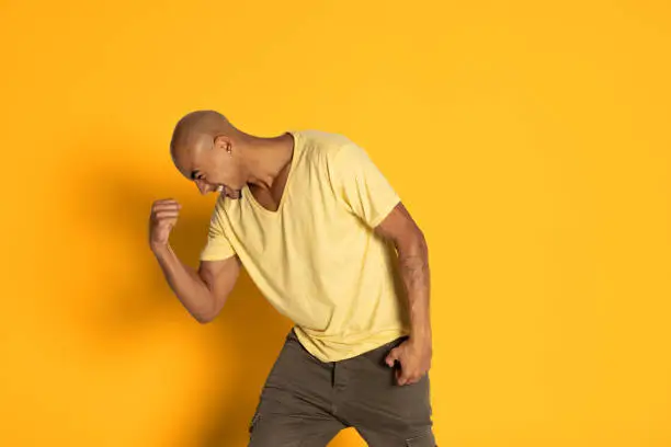 Photo of Emotional dark skinned man in t-shirt posing isolated on yellow color studio background. Concept of human emotions