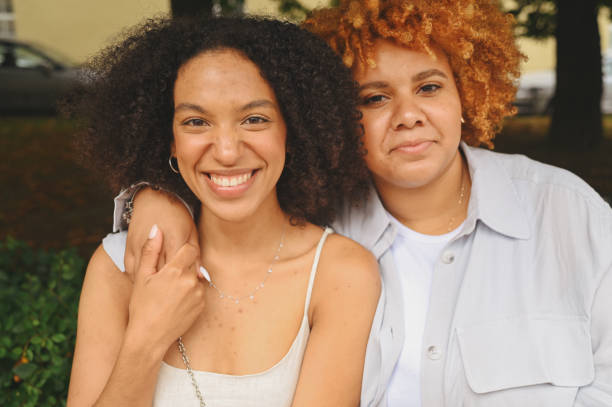 Close up portrait lovely beautiful happy lesbian African American couple hugging around city street landscape at summer. LGBT community concept. Female friends smiling enjoying love moments together stock photo