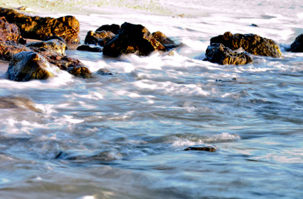 Clear sea water wave flowing through rocks on sand beach