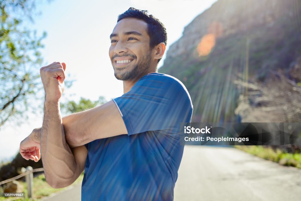 Shot of a handsome young man standing alone and stretching during his outdoor workout I stretch before and after a workout Exercising Stock Photo