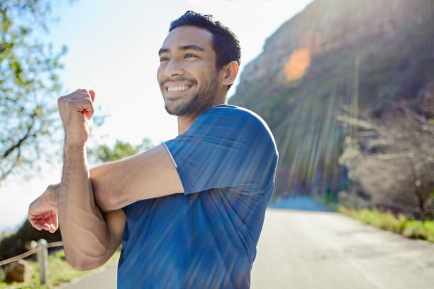 Shot of a handsome young man standing alone and stretching during his outdoor workout I stretch before and after a workout only men stock pictures, royalty-free photos & images