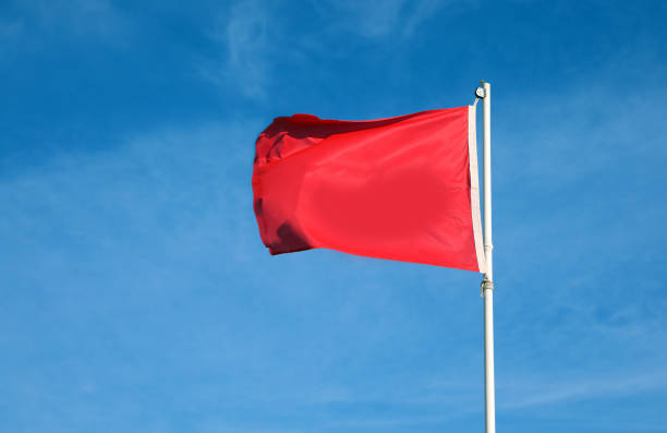 istock Red flag with blue sky waving as a warning and attention sign 1359151081