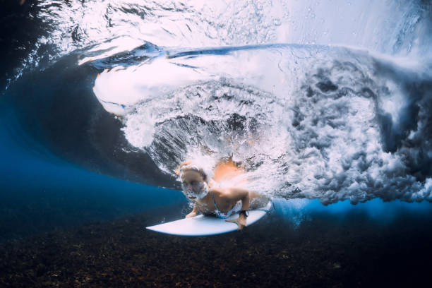 istock Woman surfer with surfboard duck dive under ocean wave. 1359152987