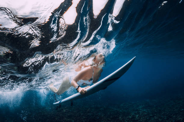 istock Surfer woman with surfboard dive under wave in blue ocean. 1359153020