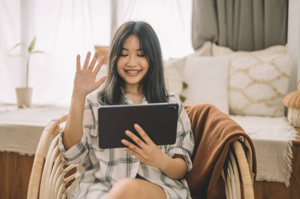 istock Smiling young Asian woman video chatting using digital tablet at home 1359155021