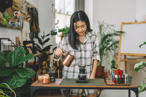Young Asian woman  pouring water on coffee ground with filter at her kitchen at home.