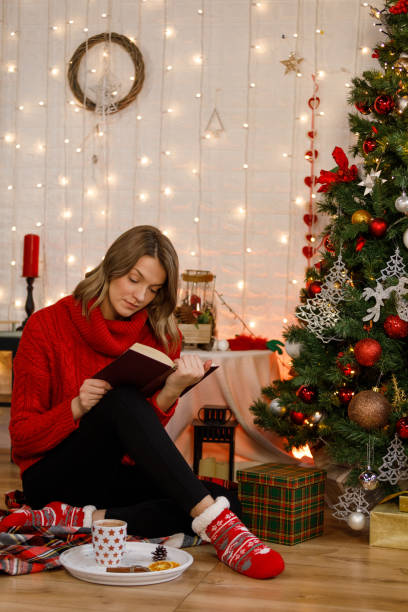 istock Young woman reading a book by the Christmas tree 1359158999