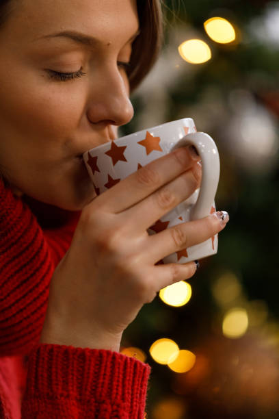 istock Young woman drinking hot chocolate by the Christmas tree 1359159328