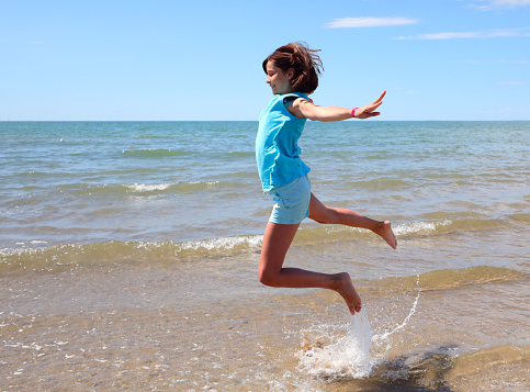young girl makes another jump on the seashore sprinkling water with barefoot feet