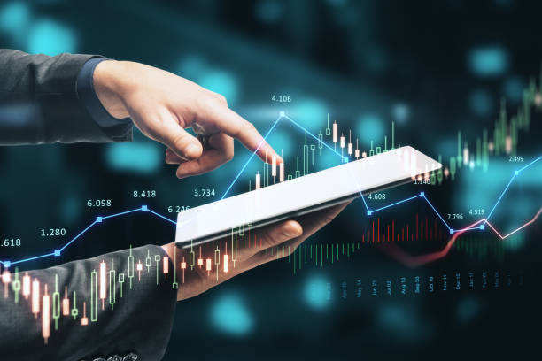 Close up of hand pointing at tablet with glowing forex chart trading interface on blurry blue bokeh circles background. Market, economy and data exchange concept. Double exposure. stock photo