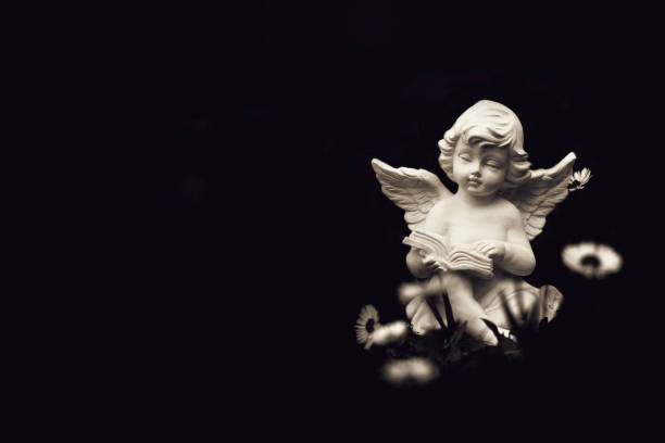 kartka kondolencyjna z aniołem siedzącym i czytającym książkę odizolowaną na czarnym tle z miejscem na kopiowanie - cherubin zdjęcia i obrazy z banku zdjęć