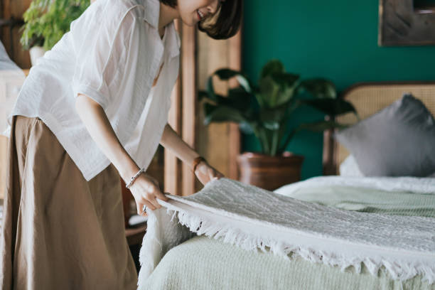 молодая азиатская женщина занимается своим утренним распорядком, застилая постель дома. давайте начнем день - home decorating стоковые фото и изображения