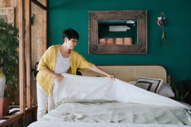 mujer asiática mayor haciendo su rutina matutina, haciendo su cama en casa. comencemos el día - making fotografías e imágenes de stock