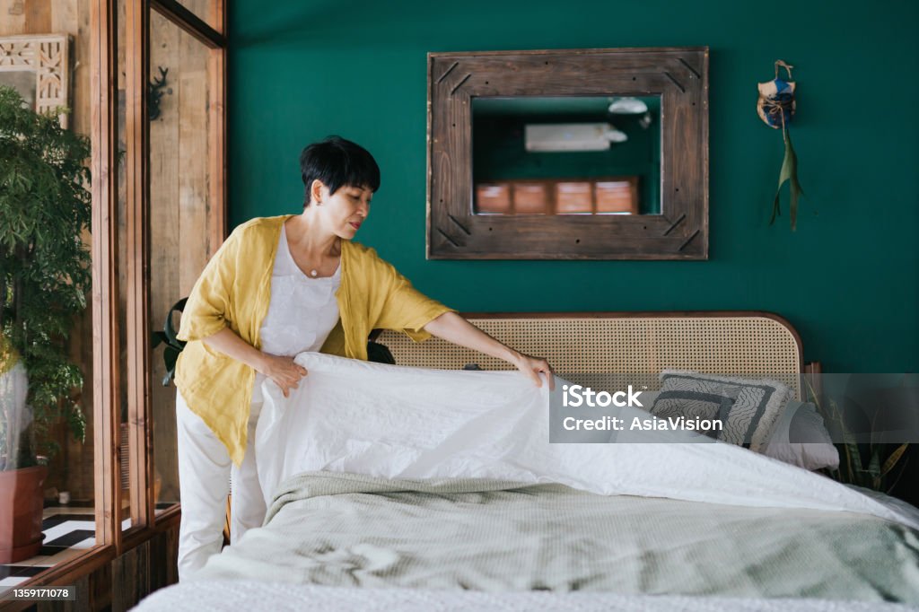 Senior Asian woman doing her morning routine, making up her bed at home. Let's get the day started Bed - Furniture Stock Photo