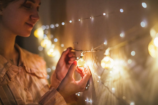 Young woman hanging Christmas lighting string as decoration