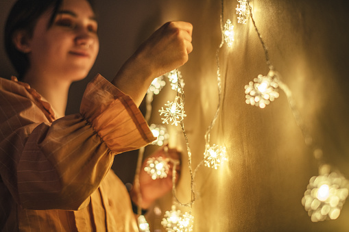 Young woman hanging Christmas lighting string as decoration