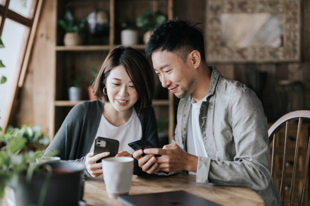 istock Happy young Asian couple having a coffee date in cafe. Drinking coffee and chatting while using smartphone together. Enjoying a relaxing moment 1359176072