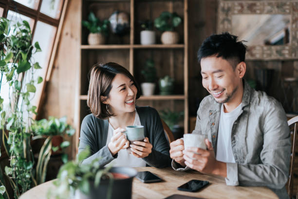 happy young asian couple having a coffee date in cafe, drinking coffee and chatting. enjoying a relaxing moment together - coffee cafe drinking couple imagens e fotografias de stock