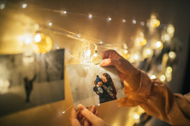 Family memories in Christmas time Young woman hanging family photos at Christmas lighting string with clothespins as decoration nostalgia stock pictures, royalty-free photos & images