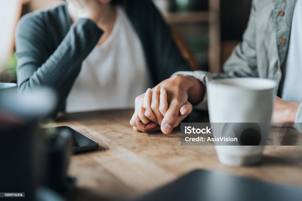 Close up of young Asian couple on a date in cafe, holding hands on coffee table. Two cups of coffee and smartphone on wooden table. Love and care concept Couple - Relationship Stock Photo