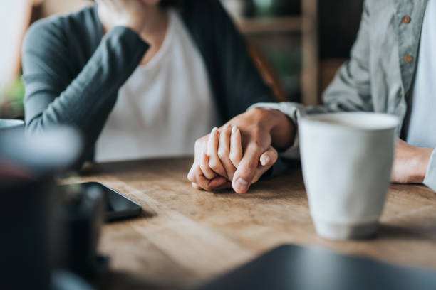 Close up of young Asian couple on a date in cafe, holding hands on coffee table. Two cups of coffee and smartphone on wooden table. Love and care concept Close up of young Asian couple on a date in cafe, holding hands on coffee table. Two cups of coffee and smartphone on wooden table. Love and care concept married stock pictures, royalty-free photos & images