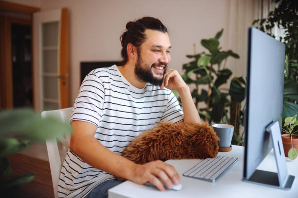 istock Man holding pet red poodle dog and using laptop at home 1359181095