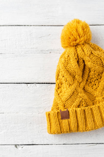 istock Yellow knitted hat on white wooden background. Top view 1359189735