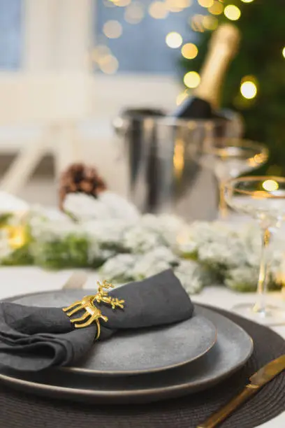 Christmas table setting with elegant empty gray plates decorated napkin ring near Xmas tree. Family holiday dinner at home. Vertical format. Close up.
