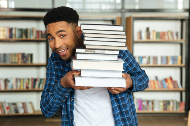 istock Young afro american male student holding stack of books 1359191047