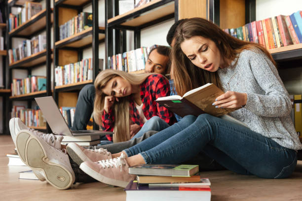 istock Tired students sitting in library on floor reading books 1359191345