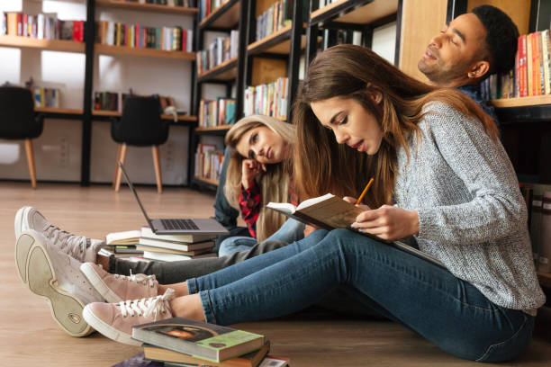 istock Concentrated students sitting in library on floor reading books. 1359193310
