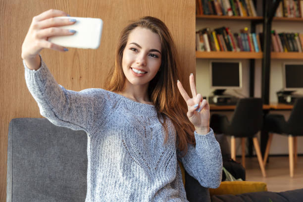 istock Smiling woman student sitting in library make selfie 1359194450