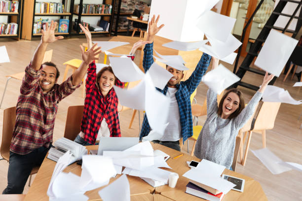 istock Happy students sitting in library throw up the paper. 1359194503