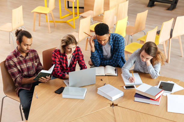 istock Concentrated students sitting in library using laptop reading books. 1359194751