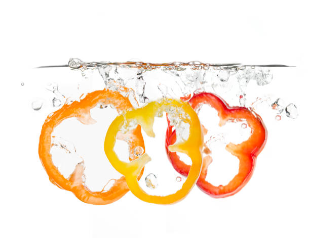 Three slices of bell pepper (orange, yellow and red) splashing into the water