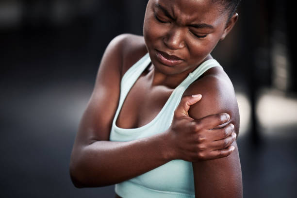 scatto di una giovane donna che tiene la spalla dolorante mentre è in palestra - shoulder pain physical injury human arm foto e immagini stock