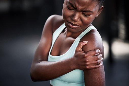 Shot of a young woman holding her shoulder in pain while at the gym