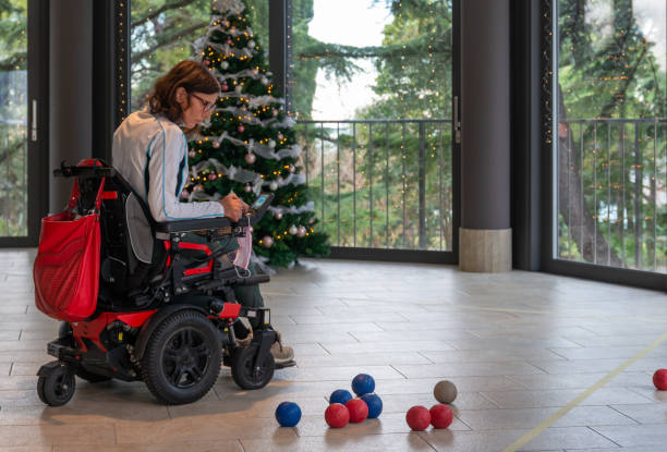 istock Two disabled people in wheelchairs play boccia next to a decorated Christmas tree with a beautiful view through the windows of the terrace of the green trees in the evil seaside resort. 1359198621