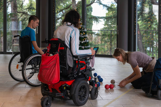 istock Two disabled people in wheelchairs play boccia next to a decorated Christmas tree with a beautiful view through the windows of the terrace of the green trees in the evil seaside resort. 1359199028