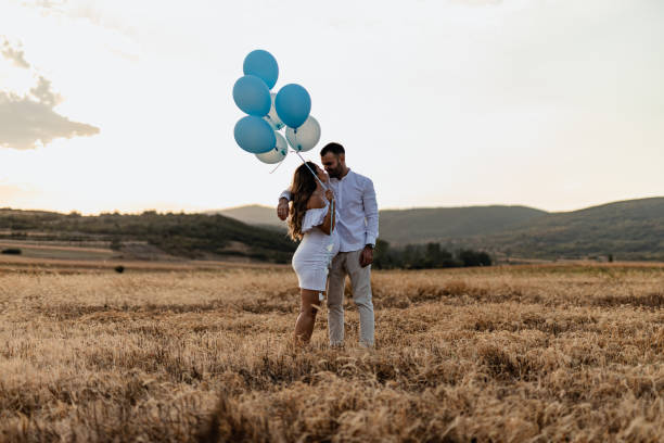 Pregnant woman and her partner revealing baby gender The happy pregnant couple, a young pregnant woman and her male partner revealing baby genre with blue balloons on a sunny summer day in nature couple hope sky blue stock pictures, royalty-free photos & images