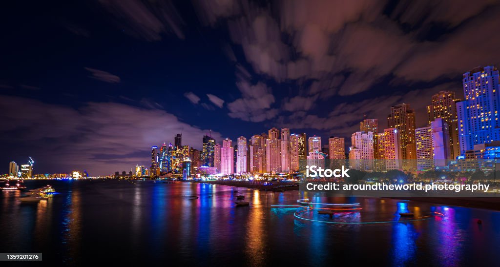 Scenic night view of the skyline of the Dubai Marina district with it's tall skyscrapers raising next to the beach and the waterfront, Dubai, UAE Dubai, United Arab Emirates, December 4th 2021: The skyline starts to live, dancing lights on the facades of the many skyscapers, as the darkness of the night sets in. Dubai Stock Photo