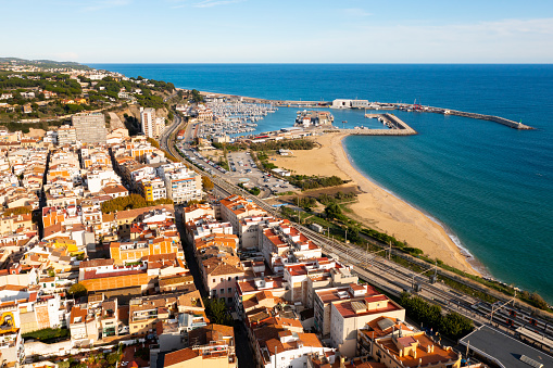 Picturesque drone view of coastal Spanish town of Arenys de Mar on bank of Mediterranean coast overlooking large sandy beach on sunny autumn day, Barcelona Province, Catalonia