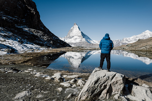 Young Caucasian man standing and looking at scenic view of lake near Matterhorn mountain in Switzerland