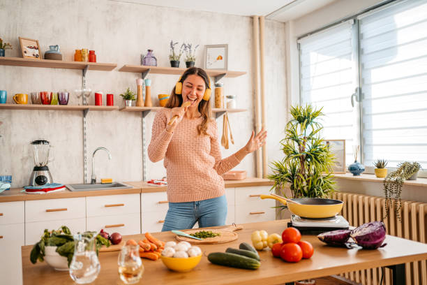 istock Young woman singing and dancing while making meal at home 1359211951