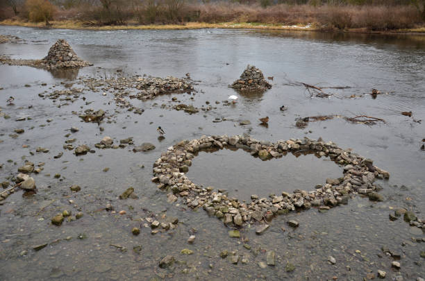 a low-flow riverbed attracts people to build mounds, hills and dams, which are broken again by waves during a flood. artificial hills and dry walls make the landscape special. heart made of stones